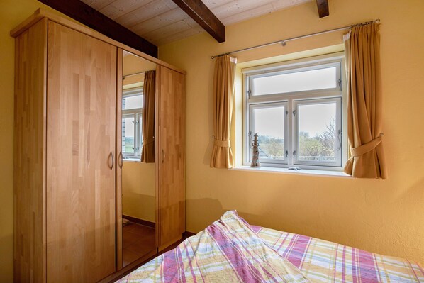 A bedroom with a bed, a window with curtains, and a wooden wardrobe.