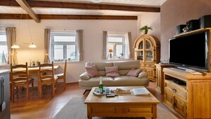 A living room with a sofa, television, wooden cabinets, and a dining area with chairs and a table. - Apartment Müllerwohnung with Terrace (Pellworm)