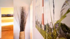 A room with a wooden ceiling, a wall-mounted painting of a lighthouse, and a vase with dried plants. - Apartment Müllerwohnung with Terrace (Pellworm)