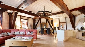 A spacious loft with a high ceiling, exposed wooden beams, a red leather sofa, a wooden coffee table, and a kitchen area with white cabinets and a dishwasher. - Apartment Inselblick with Island Views (Pellworm)