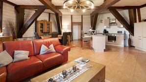 A spacious loft with a high ceiling, exposed wooden beams, a central island kitchen, and a leather sofa. - Apartment Inselblick with Island Views (Pellworm)