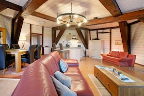 Ein großzügiges Loft mit hoher Decke, freiliegenden Holzbalken, einer zentralen Essecke, einer Küche und einer Sitzecke mit einer Couch und einem roten Sofa.