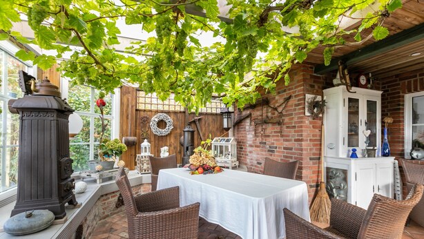 En overdækket terrasse med et bord og fletstole, murstensvægge og et træloft.