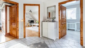 En rummelig stue med et stort spejl, trædøre og udsigt til et opholdsområde med sofa og fjernsyn.