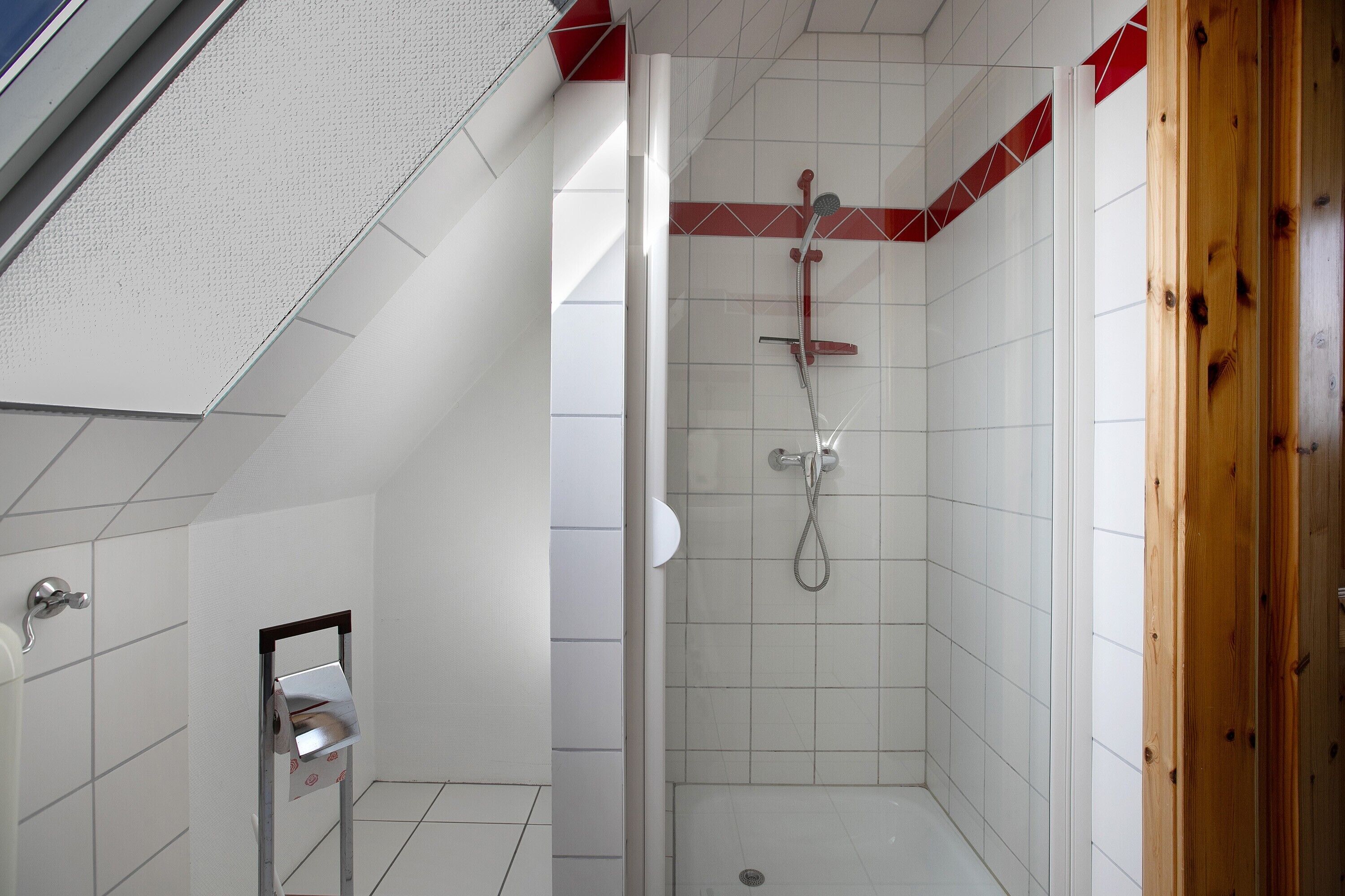 Eine Dusche mit Glastür, weiß gefliesten Wänden und einem Holztürrahmen.