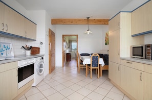 Une cuisine avec des meubles de rangement en bois, un lave-linge, une table à manger avec des chaises et un four à micro-ondes.