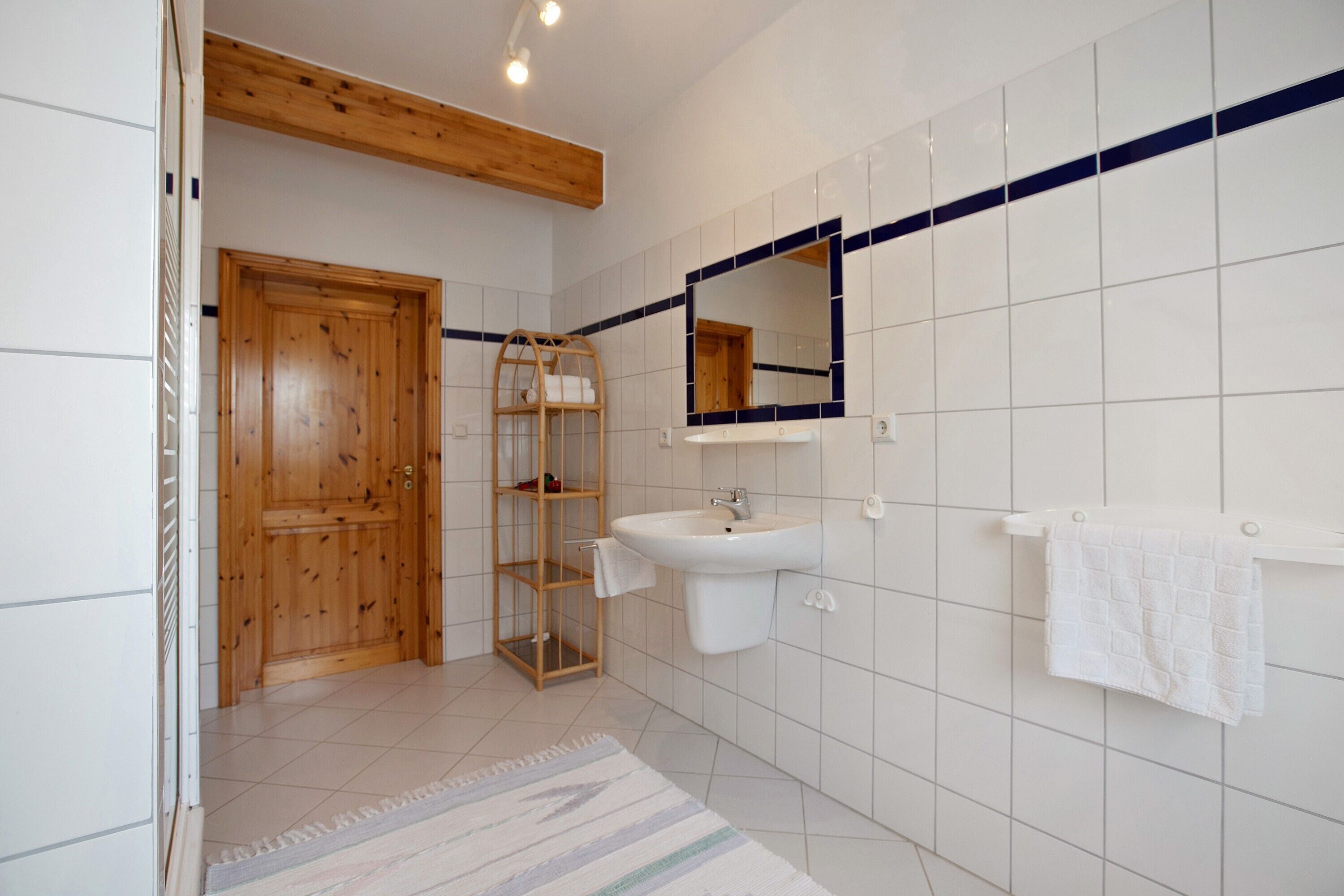 Ein Badezimmer mit Holztür, Waschbecken in Weiß, Spiegel und Handtuchhalter.