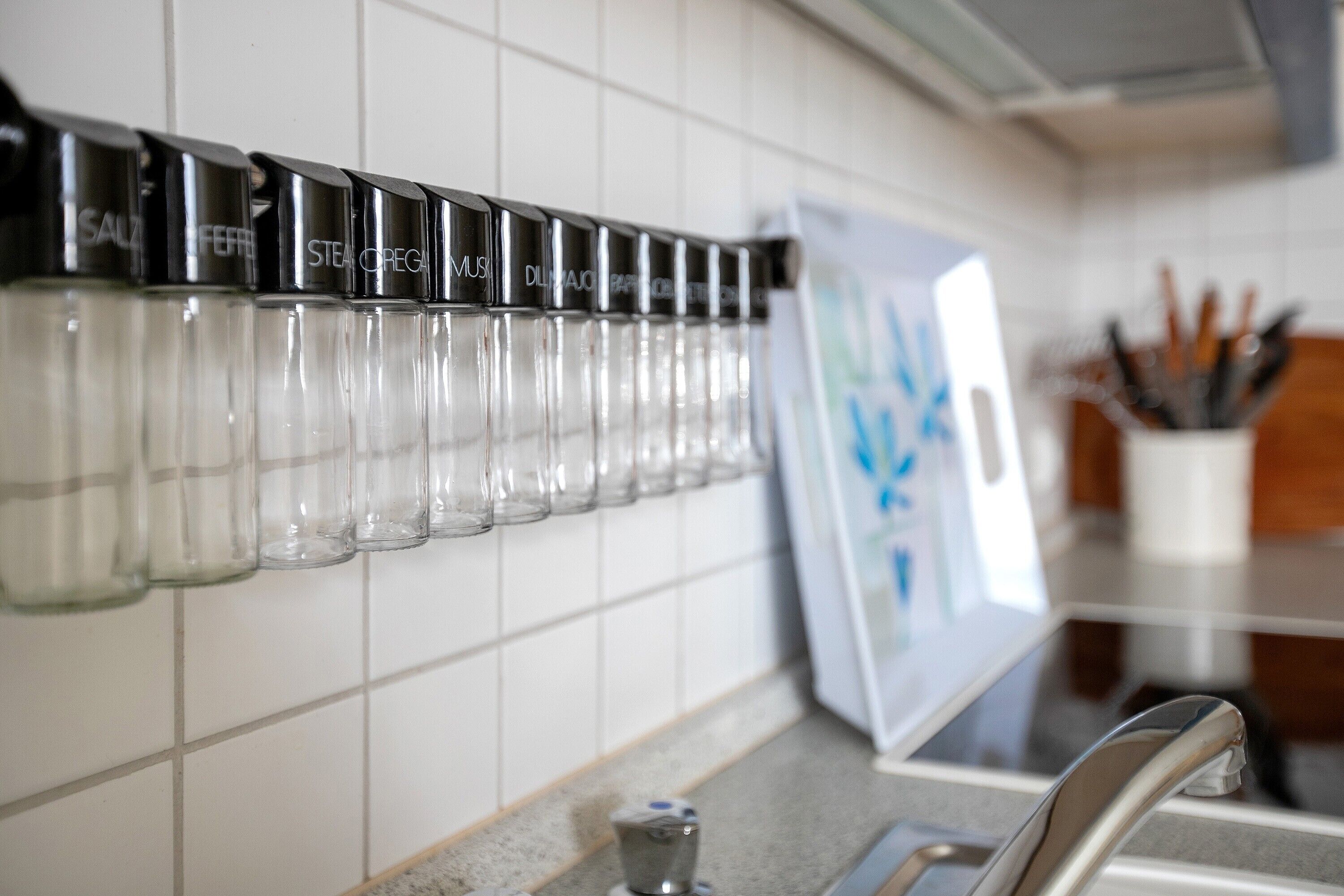 Une cuisine avec une étagère murale où sont rangées des bouteilles d’épices, un évier et un bloc à couteaux.