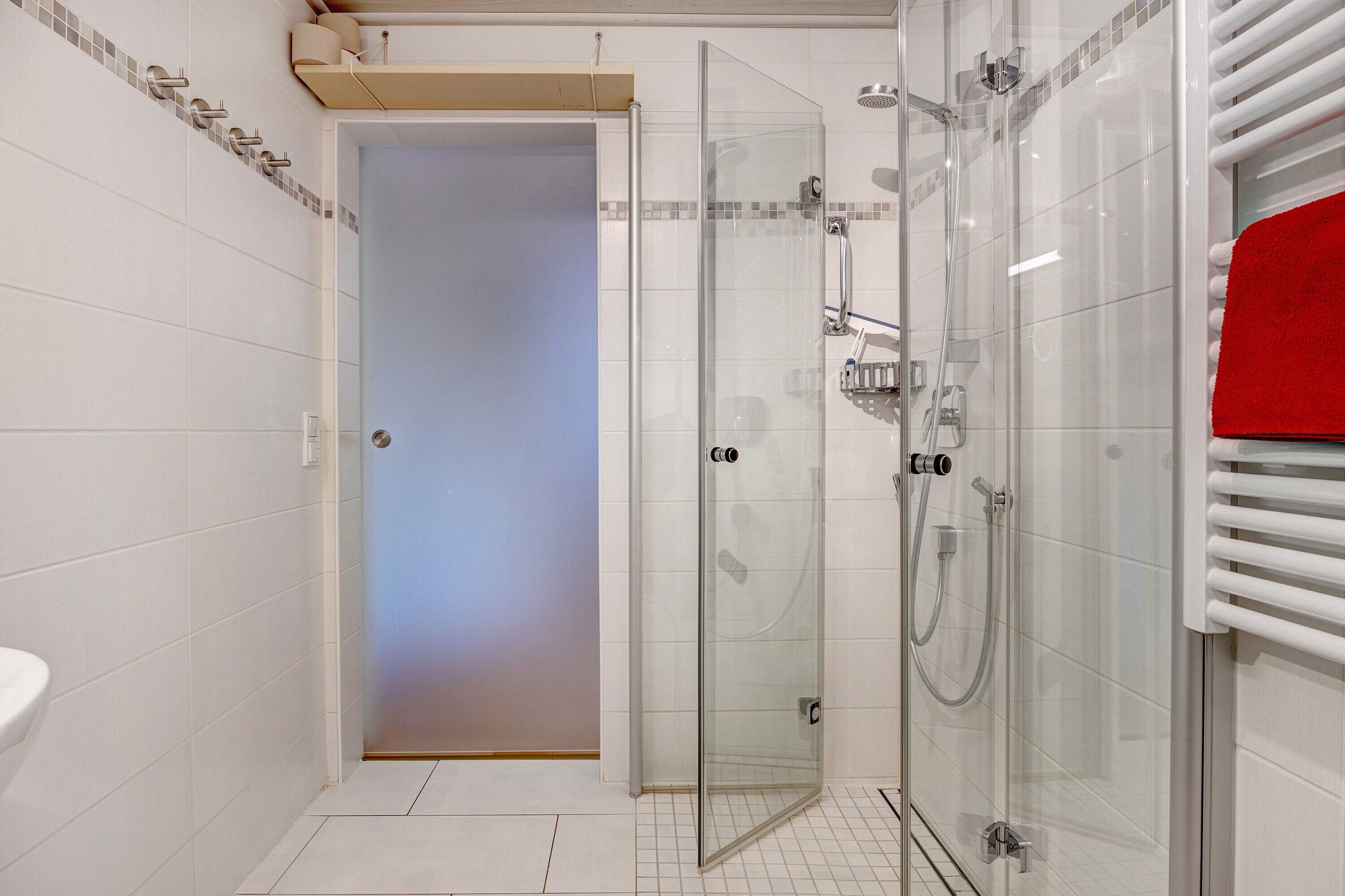Un baño moderno con cabina de ducha de vidrio, un lavabo blanco y una toalla roja.