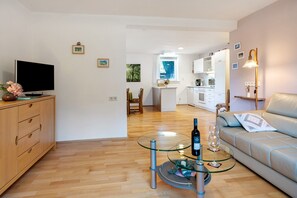 Un salon moderne avec une table basse en verre, un canapé, un téléviseur et une cuisine en arrière-plan.