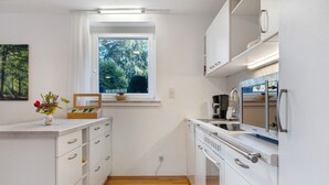 A compact kitchen with white cabinetry, a window with a view of trees, a countertop with a vase and a box, and a microwave. - Apartment Lilly with Private Terrace, Garden, and Wi-Fi (Hofgeismar)