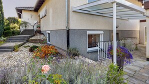 A house with a covered porch, steps leading to the entrance, and a garden with various plants. - Apartment Lilly with Private Terrace, Garden, and Wi-Fi (Hofgeismar)