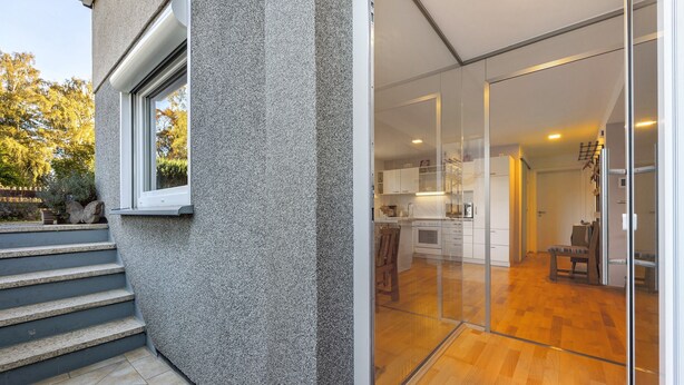 A modern house with a stone exterior, a glass door leading to a kitchen, and a wooden staircase. - Apartment Lilly with Private Terrace, Garden, and Wi-Fi (Hofgeismar)