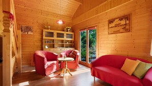 L’intérieur d’un chalet en bois est aménagé avec un canapé rouge, une petite table et une chaise. Une fenêtre offre une vue sur la verdure à l’extérieur.