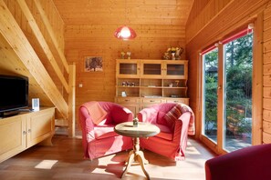 En inredning med träpanel, ett tv-appar, två rosa soffor, ett litet bord och ett skåp med glasdörrar.