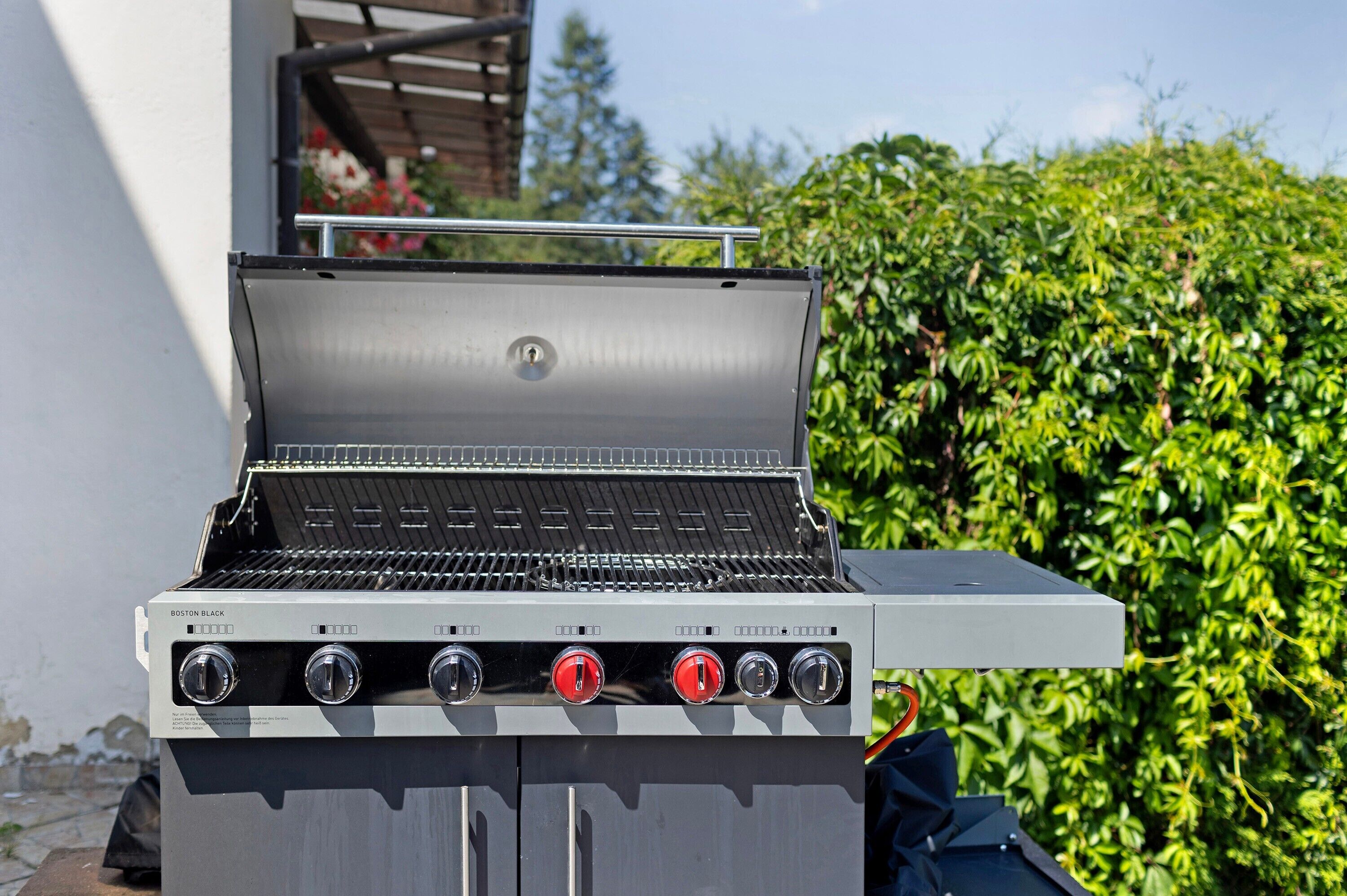 Una parrilla portátil con cuatro perillas de control, una rejilla metálica y una tapa abatible.