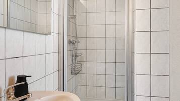 Baño con lavamanos, espejo, ducha y paredes con azulejos.