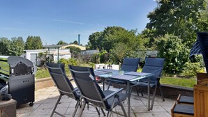 Patio esterno con barbecue, sedie e tavolo.