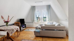 Una stanza in stile loft con pavimento in legno, un divano, una TV e un tavolo da pranzo con tovaglia floreale.