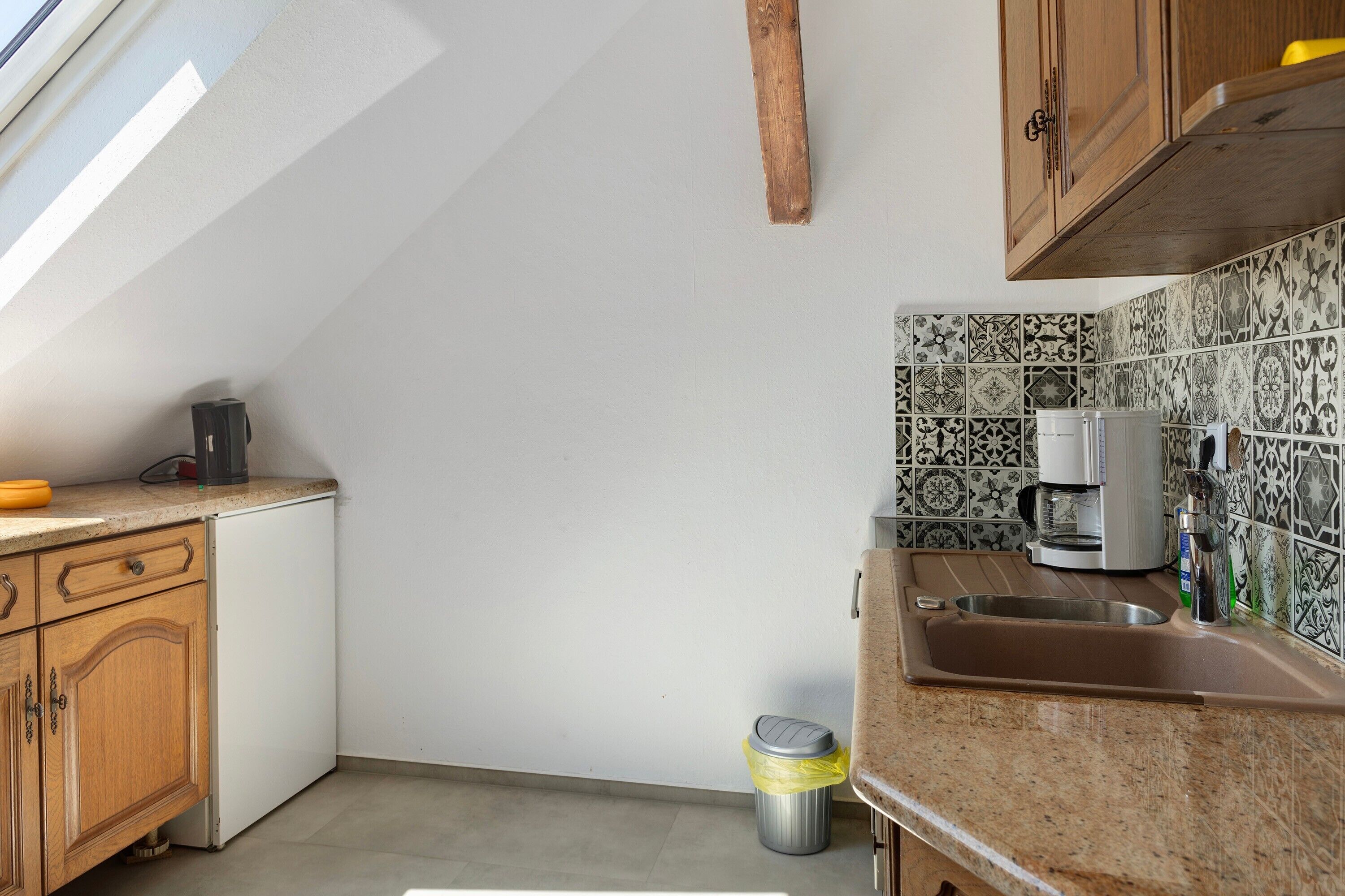 A kitchen with a window, a coffee maker, and a trash can.