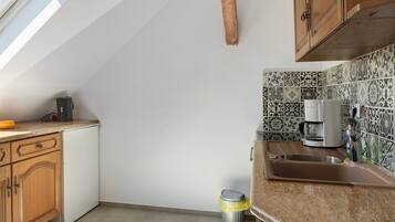 A kitchen with a window, a coffee maker, and a trash can.