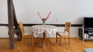 A dining table with a floral tablecloth, two wooden chairs, and a vase with flowers.