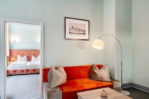 Habitación de hotel con un sofá rojo, una mesa de centro de madera, un cuadro en la pared y una lámpara de pie.