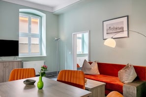 Una sala de estar moderna con una mesa de comedor, sillas naranjas, un sofá rojo y un cuadro en la pared.