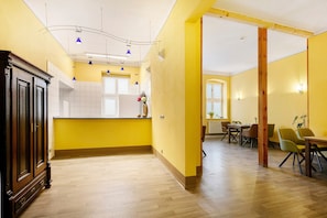 Una habitación amplia con piso de madera, una zona de cocina con armarios blancos y una zona de comedor con sillas y una mesa.