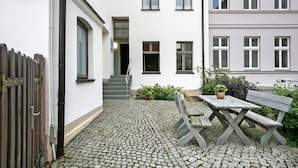 A courtyard with a wooden table and bench, a wooden fence, and a building with multiple windows and a staircase. - Apartment 'Ferienwohnung 3' with Shared Terrace and Wi-Fi (Luckau)