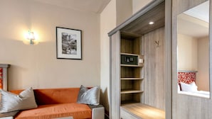A modern room with a sofa, a small table, a wall-mounted shelf, and a mirror reflecting a bed with patterned curtains. - Apartment 'Ferienwohnung 3' with Shared Terrace and Wi-Fi (Luckau)