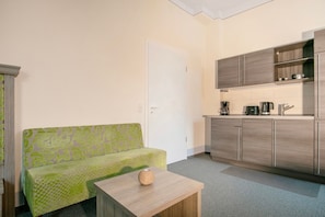A compact kitchen with a built-in stove, a dining area with a small table, and a green patterned sofa.