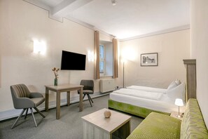 A hotel room with a bed, two chairs, a small table, a TV, a lamp, and a picture on the wall.