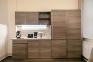 Une cuisine compacte équipée d’une cuisinière intégrée, d’une machine à café et d’une bouilloire posées sur le plan de travail.