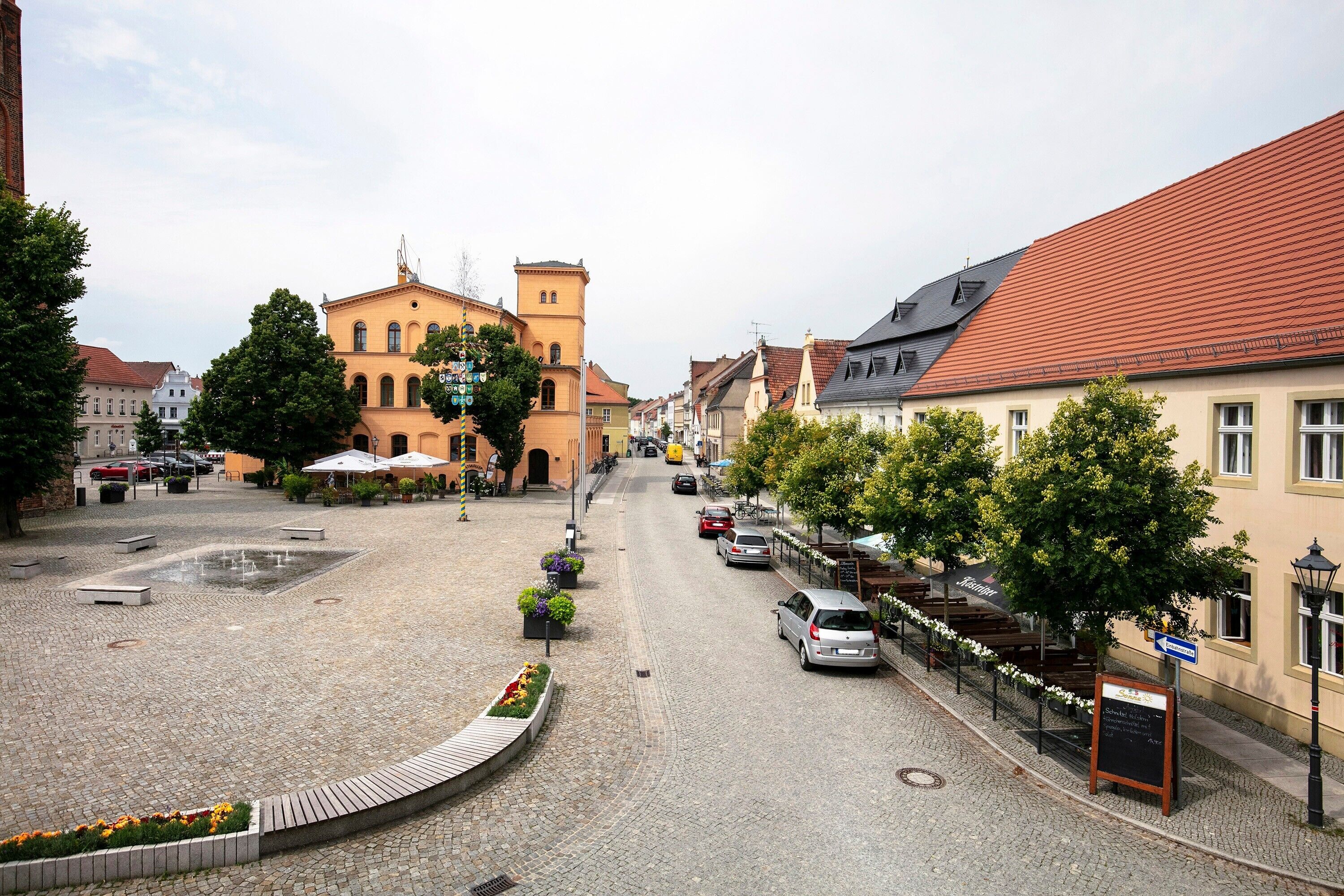 A cobblestone street with buildings, a fountain, and outdoor seating.