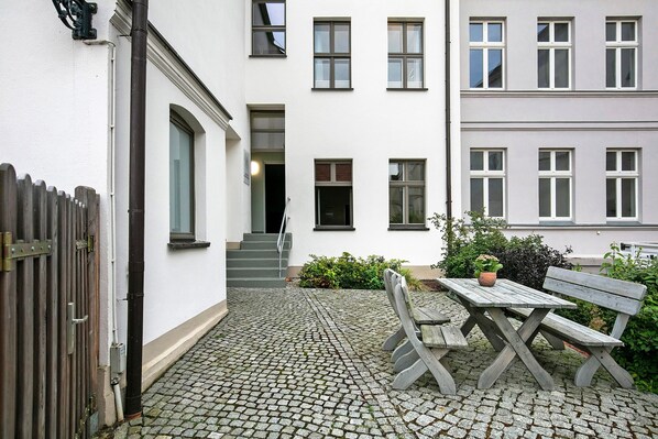 Ein Innenhof mit Holztisch und Bank, einem Holzzaun und einem Gebäude mit zahlreichen Fenstern und einer Treppe.