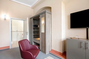 Ein Hotelzimmer mit einem roten Sessel, einem Fernseher, einem Schrank und einem begehbaren Kleiderschrank.