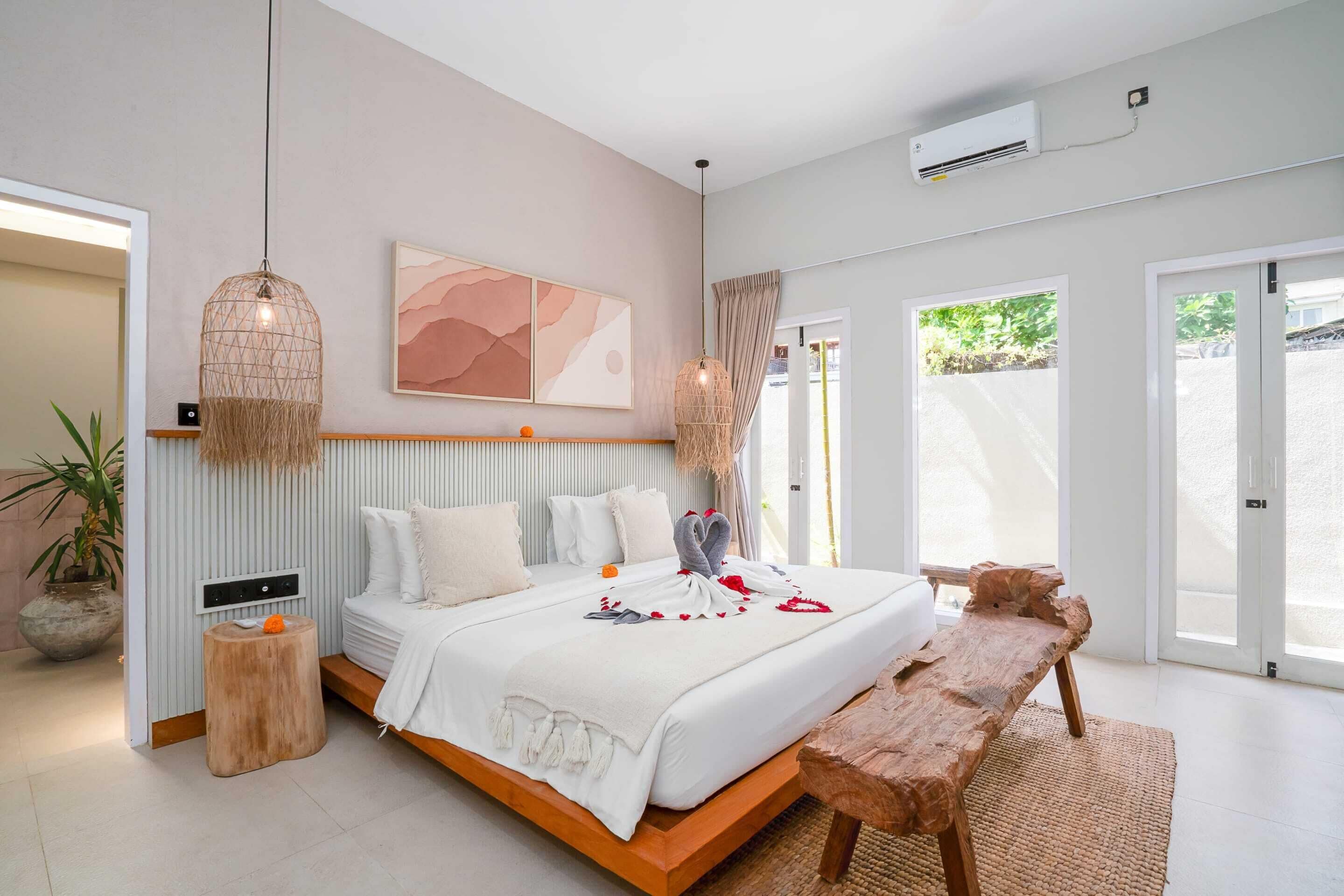 Een moderne slaapkamer met een groot bed, een houten bankje en een hanglamp.