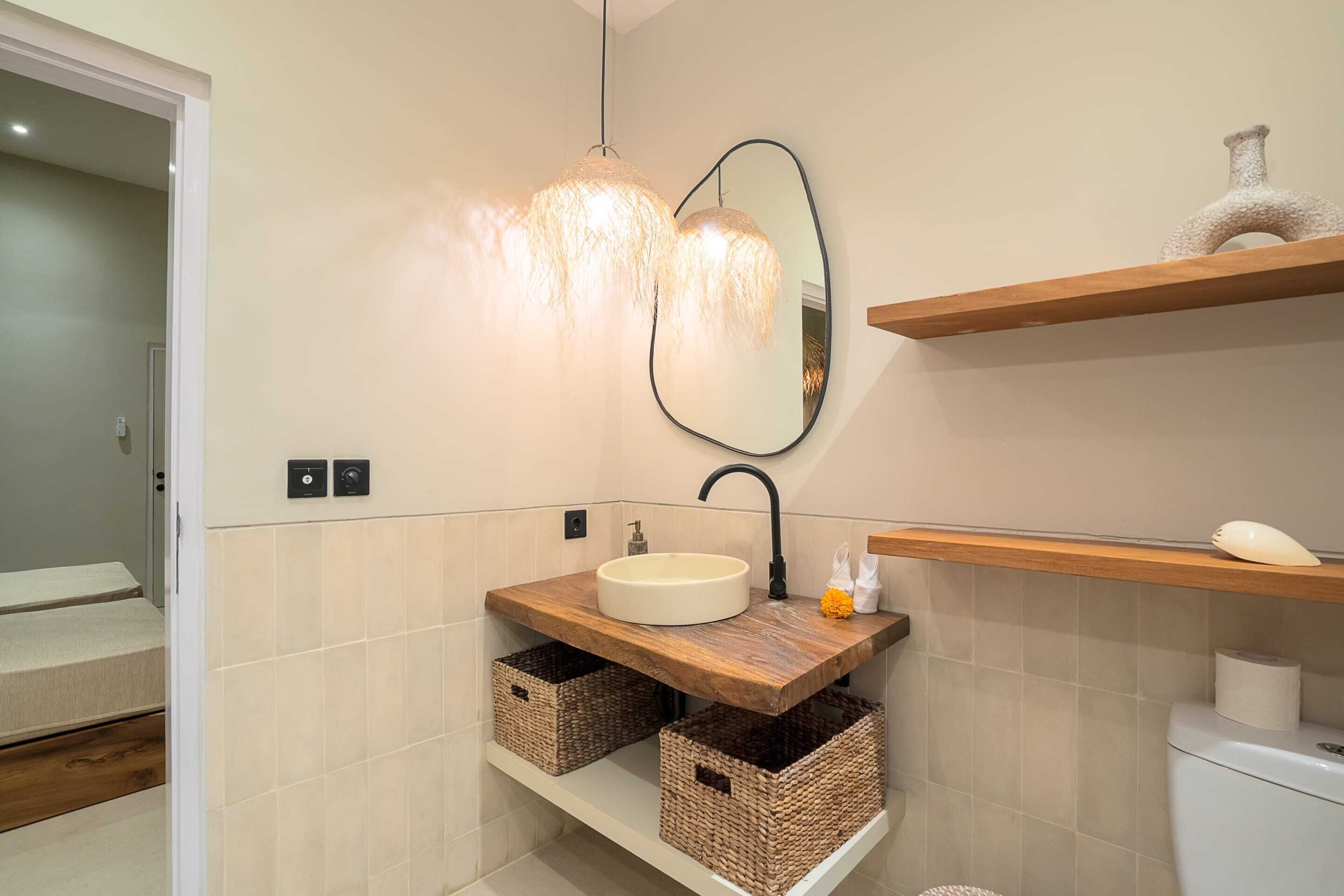 Un bagno con un lavandino rotondo, mensole in legno, cesti in vimini, uno specchio e un lampadario.