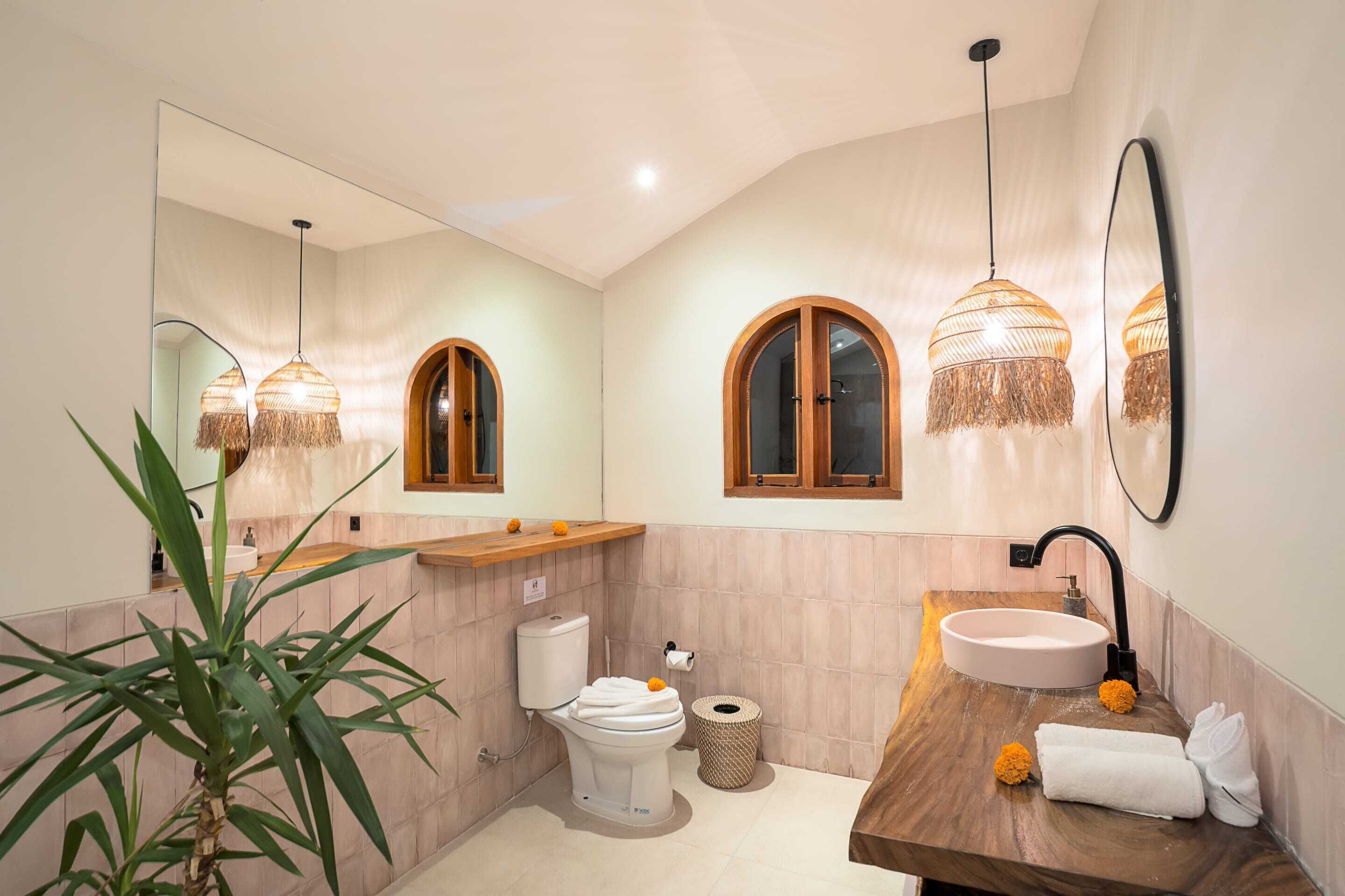 A modern bathroom with a round sink, a toilet, a large mirror, and two pendant lights.