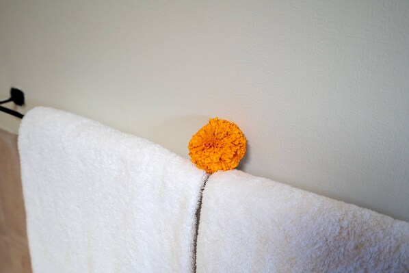 A white towel hanging on a wall with a single orange flower attached to it. - Villa Water Star (Canggu)