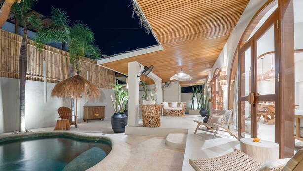 Un área de piscina interior con sillones de descanso, techo de madera y plantas en macetas.