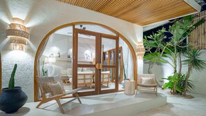 Un área de estar al aire libre con mobiliario de mimbre, una planta en maceta y un arco de madera que da a una habitación.
