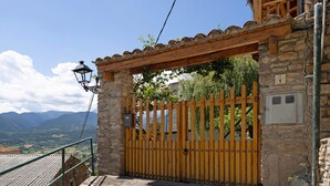 Un edificio de piedra con una puerta de madera, un muro de piedra con una placa de número y vistas a montañas.