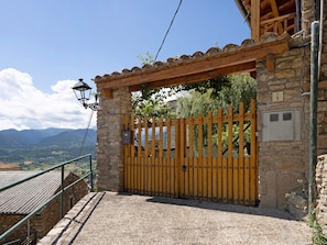 A stone building with a wooden gate, a stone wall with a number plaque, and a view of mountains.