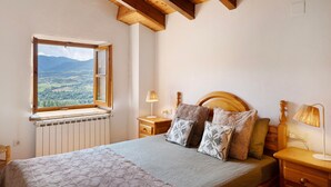 Un dormitorio con cama, cabecera de madera, mesitas de noche, lámparas, ventana con vistas y un radiador.