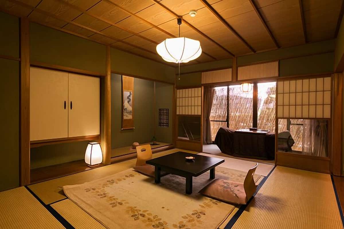 A traditional Japanese room with tatami flooring, a low table, a sofa, sliding doors, and a view of the outside.