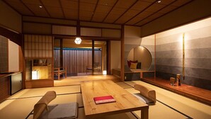 Ein traditioneller japanischer Raum mit Tatami-Bodenbelag, einem niedrigen Holztisch und einer verschiebbaren Tür zu einem weiteren Raum.