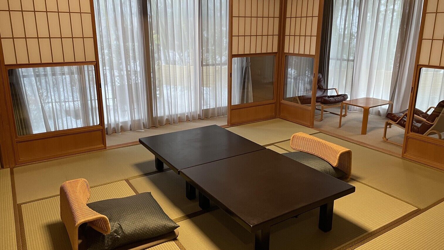 A traditional Japanese room with tatami flooring, a dark wooden table, and two tatami mats with cushions.