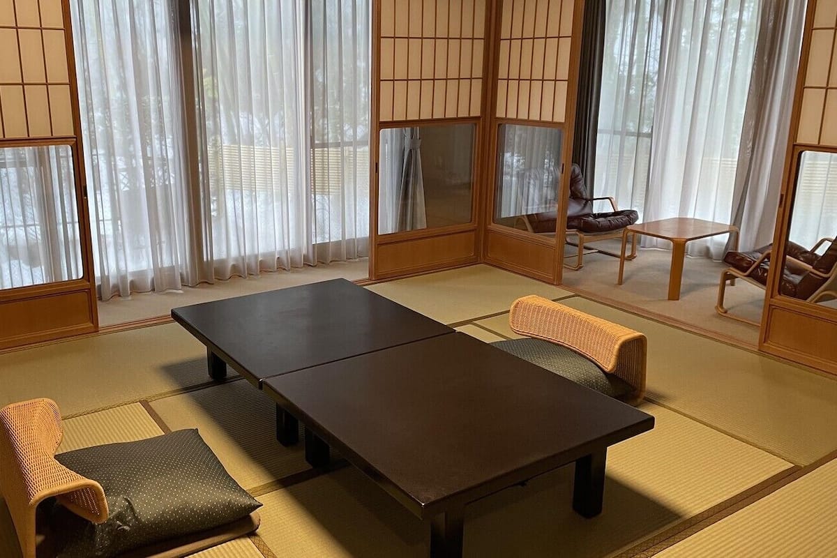 A traditional Japanese room with tatami flooring, a dark wooden table, and two tatami mats with cushions.